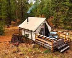 a tent set up in the woods with stairs leading to it and a grill on the porch