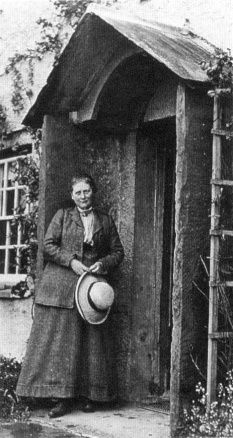 an old black and white photo of a woman standing in front of a shed