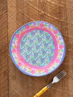 a colorful plate sitting on top of a wooden table next to a fork and knife