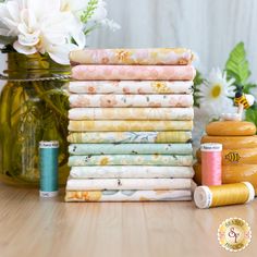 a stack of different colored fabrics next to a vase with flowers and thread on it