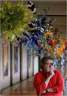 a man standing in front of a bunch of glass flowers hanging from it's ceiling