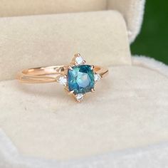 an engagement ring with a blue stone and diamonds in the middle, sitting on a white velvet box