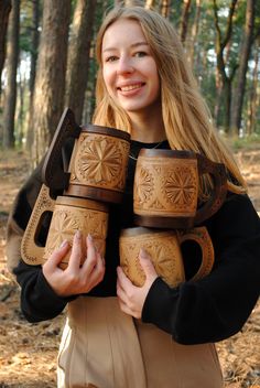 a woman is holding several wooden mugs in her hands