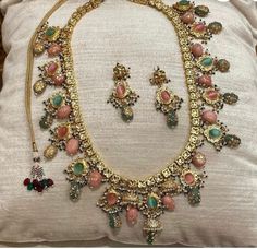 an elaborate necklace and earring set is displayed on a pillow in front of a cushion