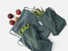 two green mesh bags filled with fruits and vegetables on top of a white surface next to each other