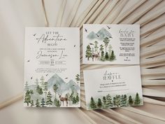 the wedding stationery is decorated with watercolor trees and mountains