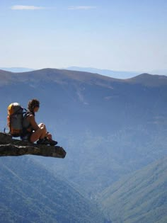 a person sitting on top of a rock with a backpack over their shoulder looking at the mountains