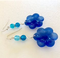 "Beautiful light sapphire blue or royal blue sea glass flowers are the feature of these pretty dangle earrings. Large 1\" sea glass flower is accented with contrasting shades of royal blue, teal and aqua blue sea glass rounds. Earrings are made of cultured tumbled sea glass and wire wrapped in German silver plated jeweler's wire. They hang from silver plated ear wires. Light sapphire blue earrings measure 2\" long and royal blue are 2 1/4\" long. Also available in Sterling silver. Listing is for Blue Flower Earrings Nickel Free, Blue Flower Jewelry For The Beach, Hypoallergenic Blue Earrings For The Beach, Blue Hypoallergenic Earrings For The Beach, Blue Flower Shaped Jewelry With Ear Wire, Blue Flower Earrings For Beach, Blue Hypoallergenic Flower Drop Earrings, Blue Hypoallergenic Drop Flower Earrings, Adjustable Blue Flower Earrings