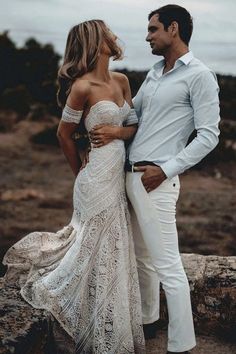 a man and woman standing next to each other on top of a rocky hill with trees in the background