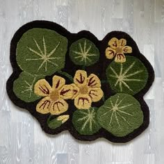 a green and yellow rug with flowers on it sitting on a wooden floor next to a white wall