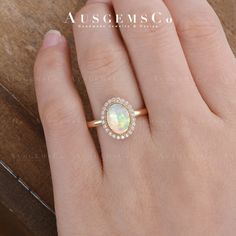 a woman's hand wearing a gold ring with an opal and diamond center