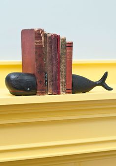 a book shelf with books and a whale statue on it's side, next to a yellow wall