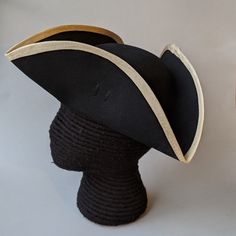 "This military style three cornered tricorn hat is made from top quality wool felt. The edges have been trimmed even and the sides held up or \"cocked\". It has been trimmed around the brim with gold fold-over braid. It is also available with black or white braid. Plain untrimmed hats are listed separately. Gold tone of edging may vary due to availability. Attached is a 3.5 \" black, pleated cockade with gold star button. The brim measures about 4.25\" to 4.5\" and the crown is about 4\" high. W Tricorn Hat, James Monroe, Star Buttons, Costume Hats, Black Hat, Military Style, Felt Hat, Gold Star, White Trim