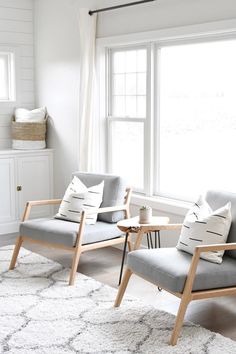 two chairs in a living room with white walls and wood trim on the windowsill