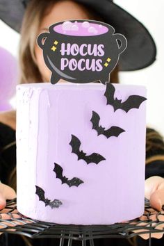 a woman holding up a cake with bats on it and a sign that says hoccus pocus