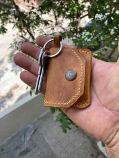 a hand holding a brown leather wallet with a keychain hanging from it's side