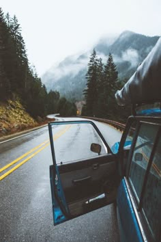 a car driving down the road with mountains in the background and foggy skies above