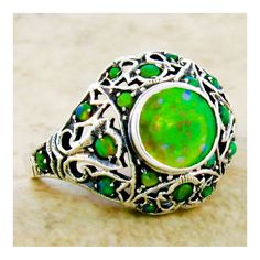 This exquisite piece is a Vintage Estate ring, featuring a green lab-created fire opal as its centerpiece, set within an intricate filigree design. Complementing the central stone are green lab-created opal accent stones, adding to the ring's overall allure. The ring is crafted from 925 solid sterling silver, ensuring both quality and durability. The dimensions of the ring are noteworthy, with the top measuring just over 1/2 inch in length, providing a substantial and elegant presence on the fin Green Opal Cabochon Ring, Elegant Green Opal Ring In Sterling Silver, Green Opal Ring Gift, Green Opal Ring As A Gift, Green Opal Ring For Anniversary, Green Opal Ring For May Birthstone Gift, Anniversary Green Opal Ring, Green Cabochon Opal Ring, Unique Green Cabochon Opal Ring