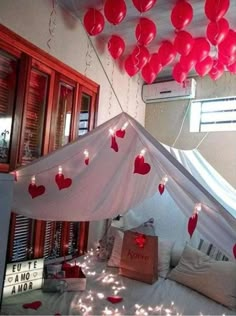 a canopy bed with red heart shaped balloons hanging from it's sides and lights on the ceiling