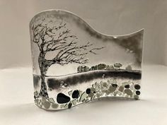 a glass sculpture with a tree and rocks in the foreground on a white background