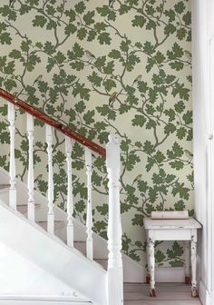 a white banister next to a wall with green leafy wallpaper on it