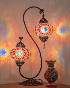 two colorful lamps sitting on top of a wooden table next to a vase and lamp shade