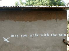 a man is standing in front of a wall with writing on it that says, may you walk with the rain