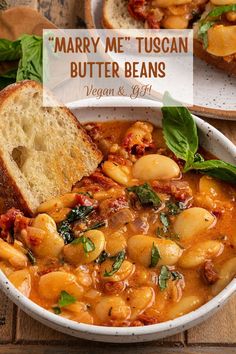 a white bowl filled with pasta and bread on top of a wooden table next to a piece of bread