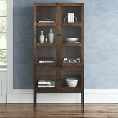 a wooden cabinet with glass doors and shelves in the corner next to a blue wall