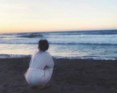 a woman sitting on top of a sandy beach next to the ocean