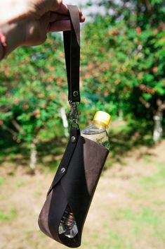 a hand holding a bottle with a lanyard hanging from it's side in front of some trees