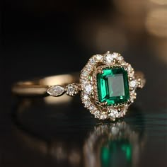 an emerald and diamond ring sitting on top of a table