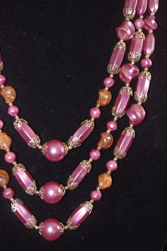 "Vintage 3 Strand Beaded Necklace: Purple Pearls & Orange Beads w/ Gold Filigree Beads, 1960s Unusual three-strand necklace with various-shaped purple pearls with gold filigree endcaps, as well as clear orange plastic beads with a slight aurora borealis sheen. A gorgeous mid-century masterpiece! Hook clasp, marked \"Hong Kong.\" The shortest strand is 20\" long, but with the expander is is 22.5\" long." Vintage Beaded Necklaces With Colorful Beads, Vintage Necklaces With Large Beads For Party, Vintage Beaded Necklace With Round Beads For Party, Vintage Party Necklaces With Large Beads, Vintage Large Beads Necklaces For Party, Vintage Beaded Party Necklace, Vintage Party Necklace With Large Beads, Vintage Round Beads Necklace For Party, Vintage Round Beaded Necklace For Party