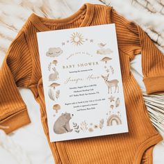 a baby shower is shown on top of a bed with an orange sweater and brown bear