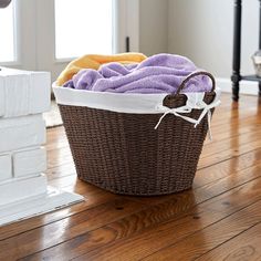 a basket filled with purple and yellow towels on top of a wooden floor next to a window