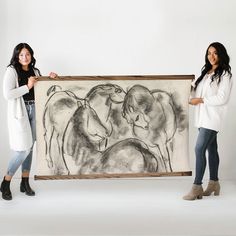 two women standing next to a drawing of horses on a white background with one holding the frame