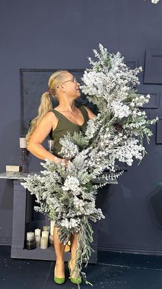 a woman standing in front of a fireplace holding a white christmas tree with snow on it