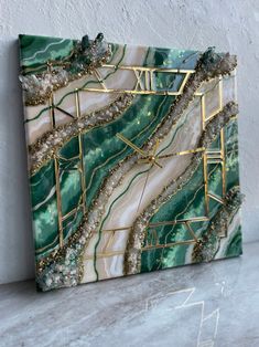 a green and white marble with gold accents on the edges is displayed in front of a wall