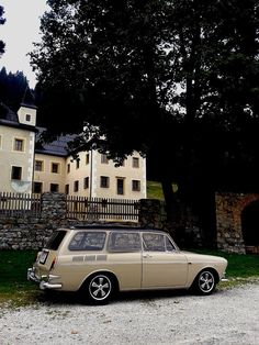 an old station wagon parked in front of a large house with stone walls and trees