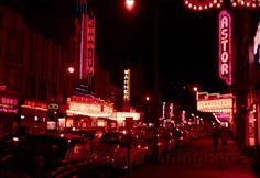 a city street at night with neon signs and parked cars