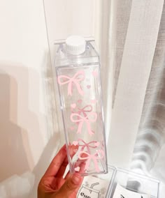 a person holding up a clear water bottle with pink bows on the front and side