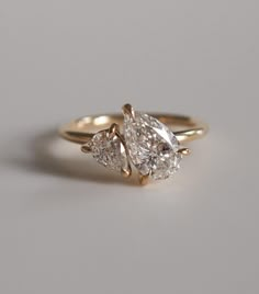 two pear shaped diamond engagement rings on a white surface, with the top one in yellow gold