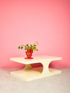 a white table with a plant on it in front of a pink wall and floor