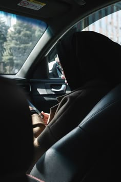 a person sitting in the back seat of a car talking on a cell phone while wearing a hood