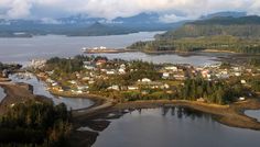 an aerial view of a small town on the water's edge with mountains in the background