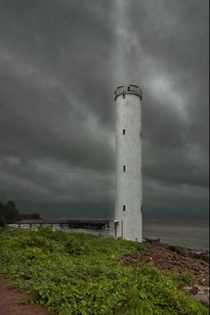 a white light house sitting on top of a lush green hillside next to the ocean