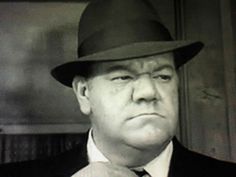 a man in a suit and tie wearing a fedora looking at the camera with an angry look on his face