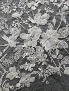 an embroidered fabric with white flowers and leaves on grey background, close up view from the bottom