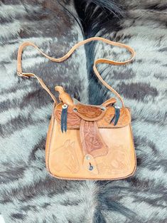 This genuine leather saddle purse is an absolute must-have! It's modeled after a saddle for a truly unique design. Plus, it features an adjustable shoulder strap so you can adjust the fit. An out-of-the-box way to accessorize with flair! Tooled Leather Saddle Purse: Measures appx. 10" x 9" x 4". Crafted of genuine leather. Available in tan & brown. Comes with adjustable strap. Made in Mexico. Weight: 2 lbs. Visit us on Facebook for inspirational ideas on decorating any space. Don't forget to fol Hand Tooled Leather Saddle Bag For Everyday Use, Leather Backed Saddle Shoulder Bag, Western Style Shoulder Bag For Everyday, Hand Tooled Leather Satchel Saddle Bag, Hand Tooled Crossbody Satchel, Saddle Bag With Detachable Strap For Daily Use, Travel Saddle Bag With Adjustable Strap, Daily Use Saddle Bag With Adjustable Strap, Hand Tooled Saddle Bag Satchel For Daily Use