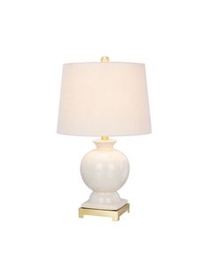 a white table lamp with a beige shade on the base and a gold frame around it